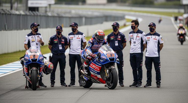 Brazilian riders on a racing circuit at dusk with cheering crowds and flags.